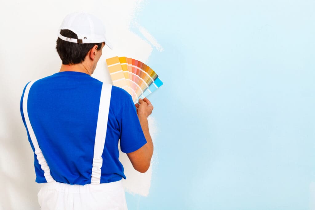 rear view of painter man looking a color palette on half painted wall, with copy space